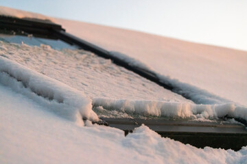 Snow-covered skylight window on villa roof with accumulated frost and melting snow in winter at sunset. Sweden.