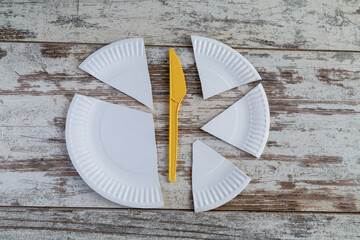 A divided white paper plate and a plastic knife arranged as clock elements symbolize limited time for eating, strict diets, and awareness of the consequences of using disposable tableware.
