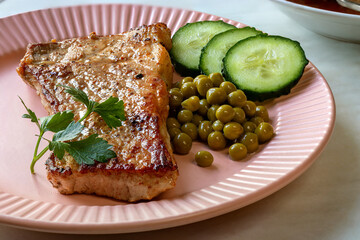 Freshly cooked pork chop. Focus Stacking. Pork chop. Pink plate, garnished with green peas, slices of fresh cucumber, sprig of parsley