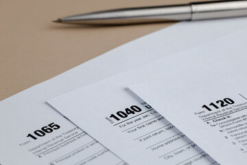 Tax season preparation with forms 1040, 1065, and 1120, and a pen on a beige table for filing tax...