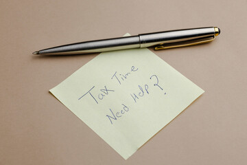 Tax season reminder with a pen resting on a sticky note: "Tax Time, Need Help?", signaling potential need for assistance with tax preparation.