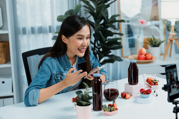 Smiling young beautiful Asian reviewing tasty mixed strawberry and cherry juice detox drinks,...