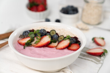 Presented by fruits putting yogurt toppings with strawberry, berry, oats, raisins and chia seed decorated by peppermint in white blow. Pink background. Set of healthy dairy product choice. Pecuniary.