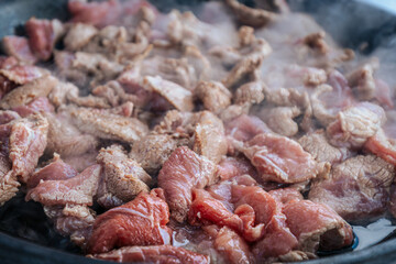Freshly sliced beef is sizzling in a hot pan, with steam rising as the meat cooks. The mixture of raw and browned pieces highlights the cooking process and the release of rich flavors.