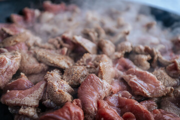 Freshly sliced beef is sizzling in a hot pan, with steam rising as the meat cooks. The mixture of raw and browned pieces highlights the cooking process and the release of rich flavors.