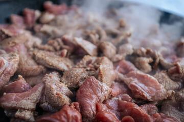 Freshly sliced beef is sizzling in a hot pan, with steam rising as the meat cooks. The mixture of raw and browned pieces highlights the cooking process and the release of rich flavors.