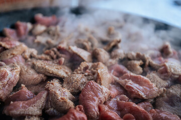 Freshly sliced beef is sizzling in a hot pan, with steam rising as the meat cooks. The mixture of raw and browned pieces highlights the cooking process and the release of rich flavors.