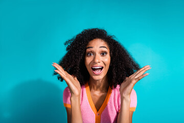 Portrait of a cheerful young woman with afro curls smiling brightly against a vibrant turquoise...