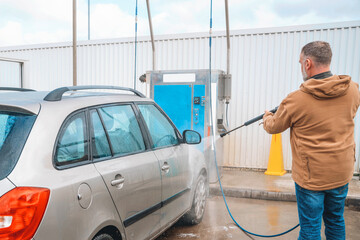 Man washes his car at a self-service car wash station in bright daylight