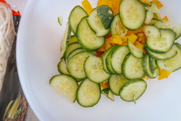 A close-up of freshly sliced cucumbers and yellow bell peppers in a white bowl. The vibrant green and yellow colors highlight the freshness of the ingredients, ready for a salad or dish.