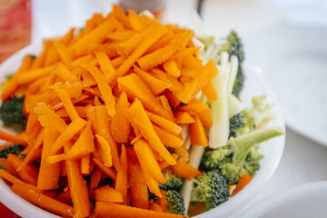 A close-up of a bowl filled with freshly chopped carrots, broccoli, and bamboo shoots. The vibrant orange and green colors highlight the fresh ingredients, ready for cooking or serving.