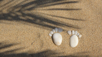 White pebbles in feet soles shape on sand of the beach