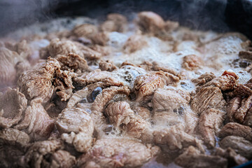 Steaming pieces of beef are being boiled or simmered in a pan, with bubbles forming around the tender meat. The heat and moisture highlight the cooking process and texture of the beef.