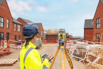 Woman Construction worker using a tablet to survey a residential development site with new houses under construction in bright safety gear