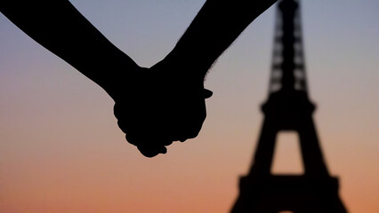 Young couple lovers joining hands in front of Eiffel tower Paris, silhouettes at sunset