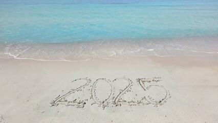 2025 written on beach sand, clear turquoise sea water, tropical exotic holiday
