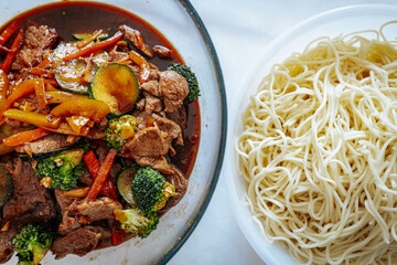 A delicious beef stir-fry with colorful vegetables in a savory sauce, served alongside a bowl of cooked noodles. A flavorful Asian-inspired meal ready to be enjoyed.