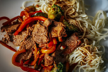 A plate of stir-fried beef with vegetables, including red bell peppers, broccoli, and zucchini, served with noodles in a savory sauce. A delicious and colorful Asian-inspired dish.