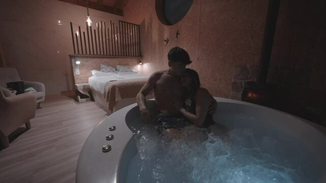 Sensual couple tenderly embracing, caressing each other inside elegant hydromassage bathtub, sharing intimate connection within luxurious hotel room's romantic atmosphere