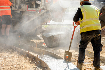 Construction workers pouring concrete for a pathway in a busy outdoor site during daylight with...