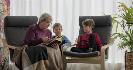Grandkids and grandmother reading a book at home