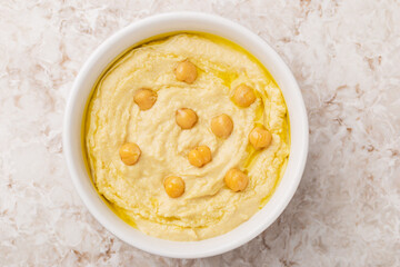 Top view on homemade hummus with chickpeas, olive oil in a white bowl on a light stone background. Traditional Arabic snack.
