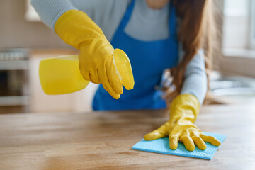 Cleaning kitchen surfaces using yellow gloves and spray cleaner during daylight hours