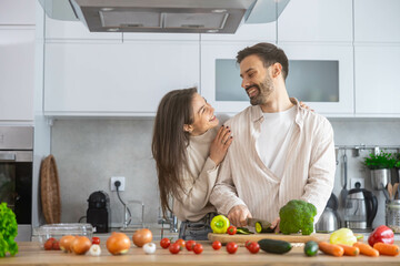 This image showcases a couple enjoying cooking moments together while smiling in their beautifully arranged kitchen.