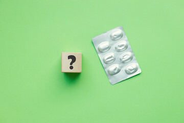 Question mark on cube and pillsmedicines on green background. Concept of medical issues