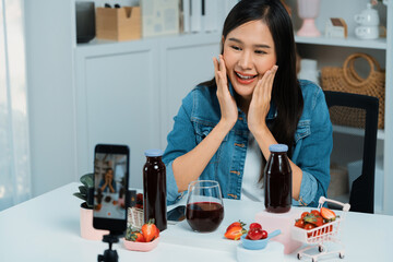 Smiling young beautiful Asian reviewing tasty mixed strawberry and cherry juice detox drinks,...