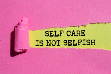 Self care is not selfish message written on ripped torn pink paper on yellow background. Conceptual...