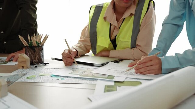 Smart architect and safety engineer discussion about building blueprint on table with architectural document, measurement tools and wooden block scatter around at modern office. Closeup. Delineation.