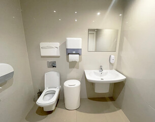 White bathroom in the medical center with toilet, washbasin, paper towels, mirror and trash can