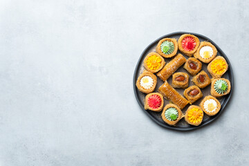 Assorted Middle Eastern sweets on a black plate. Colorful pastries with nuts and syrup. Placed on a light grey background. Traditional festive dessert.