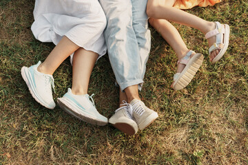 Three family members relaxing on grass showing legs and different shoes.