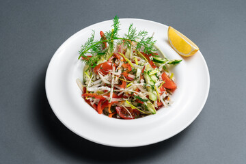 Fresh salad prepared with chopped vegetables and herbs served with a slice of lemon on a white plate