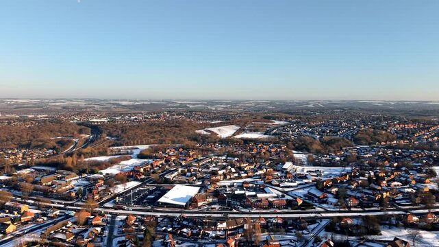 Aerial futage of Stunning winter landscape reveals a snow-covered town with hills and winding roads in the background on a clear day