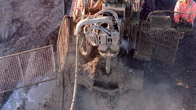 Aerial futage of Heavy construction machinery piling rig dilling into the ground at a construction site rotating and emitting mud and steam 