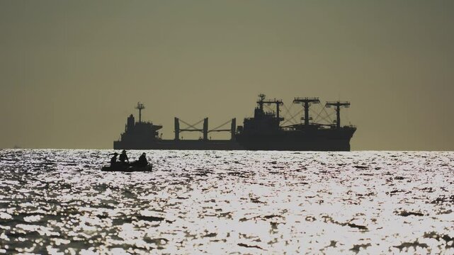 pirates on inflatable boat are about to attack tanker or bulk carrier on high seas. Silhouettes of sinister, unrecognizable Somali pirates.