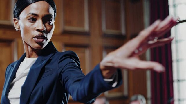 Confident female lawyer making stop gesture with hand while giving closing argument speech at court of law, courtroom with wooden panels and jury in background