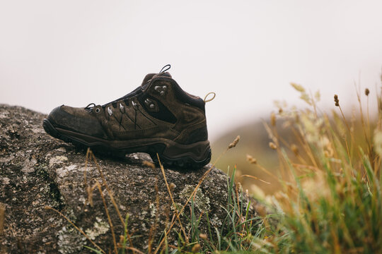 Sturdy brown hiking boot on rock in grassy outdoor setting - Powered by Adobe
