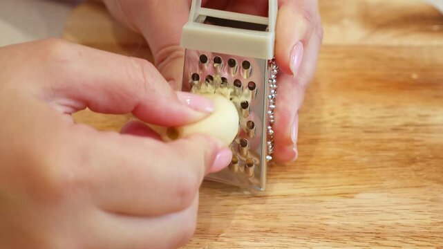 Female hands grating garlic with a small metal grater close up