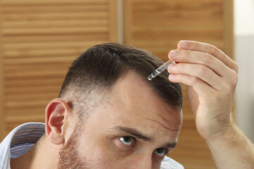 Obraz premium Baldness treatment. Man applying serum onto hair at home, closeup