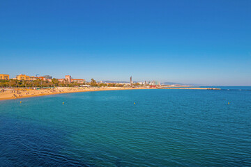 Port Olímpic Marina in Barcelona on a sunny day, featuring luxury yachts, clear blue skies, and a vibrant waterfront atmosphere along the Mediterranean coast.