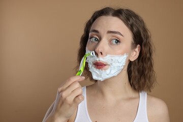 Funny woman shaving facial hair with razor on beige background. Space for text