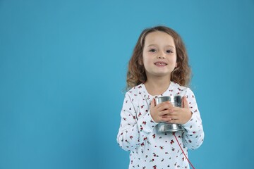 Girl using tin can telephone on blue background. Space for text