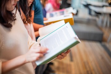 People reading books in a library. Diverse group, books in hand, reading together. Focus on reading, books, and learning in a library setting. Asian young woman reading a book.