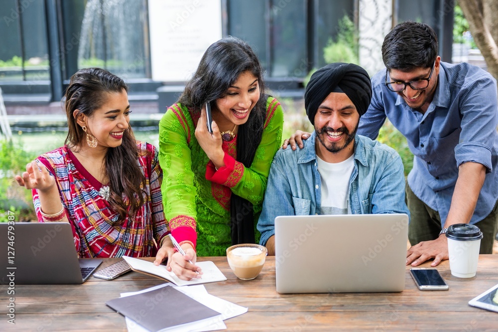 Poster group of four people collaborating at a table with laptops and notebooks, smiling and engaged in tea