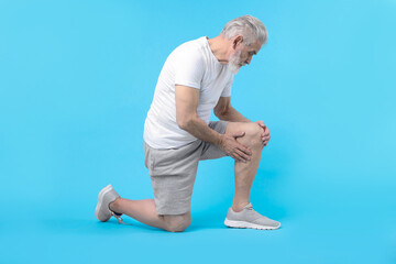 Senior man suffering from pain in his knee on light blue background