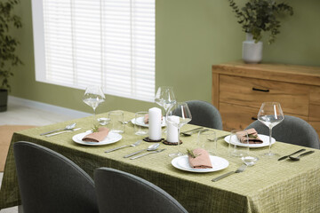 Stylish table setting with olive tablecloth, glasses and candles indoors